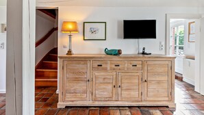 Un mueble de madera con cajones, un televisor montado en la pared, un cuadro enmarcado y una lámpara.