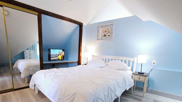 A bedroom with a large mirror, a bed, a bedside table with a lamp, and a television on a stand.