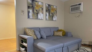 A modern living room with a grey sofa, decorative pillows, a patterned rug, and abstract wall art. - Comfy 2 bedroom condo with 75” smart TV (Chicago Ridge)