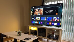 A flat-screen TV on a wooden stand with a remote control on a table in front. - Comfy 2 bedroom condo with 75” smart TV (Chicago Ridge)