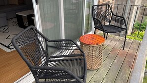 A balcony with two black wicker chairs, a small round wooden table, and a wicker basket. - Comfy 2 bedroom condo with 75” smart TV (Chicago Ridge)