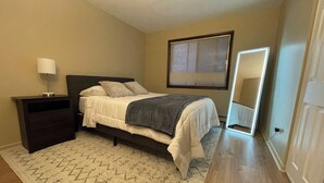 A bedroom with a bed, nightstand, lamp, and a large mirror. - Comfy 2 bedroom condo with 75” smart TV (Chicago Ridge)