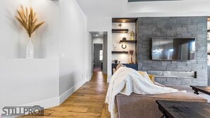 A modern living room with a stone accent wall, a mounted TV, and a wooden floor. - Ivins Oasis : Private Hot Tub & Pool (Ivins)