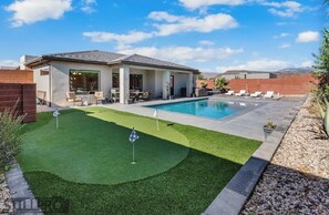 A modern house with a swimming pool, a patio with chairs, and a well-maintained lawn.