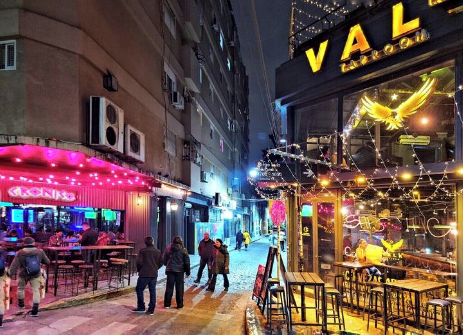 En gatuscen med en bar som heter ”VALLE” och en restaurang med neonreklamer.