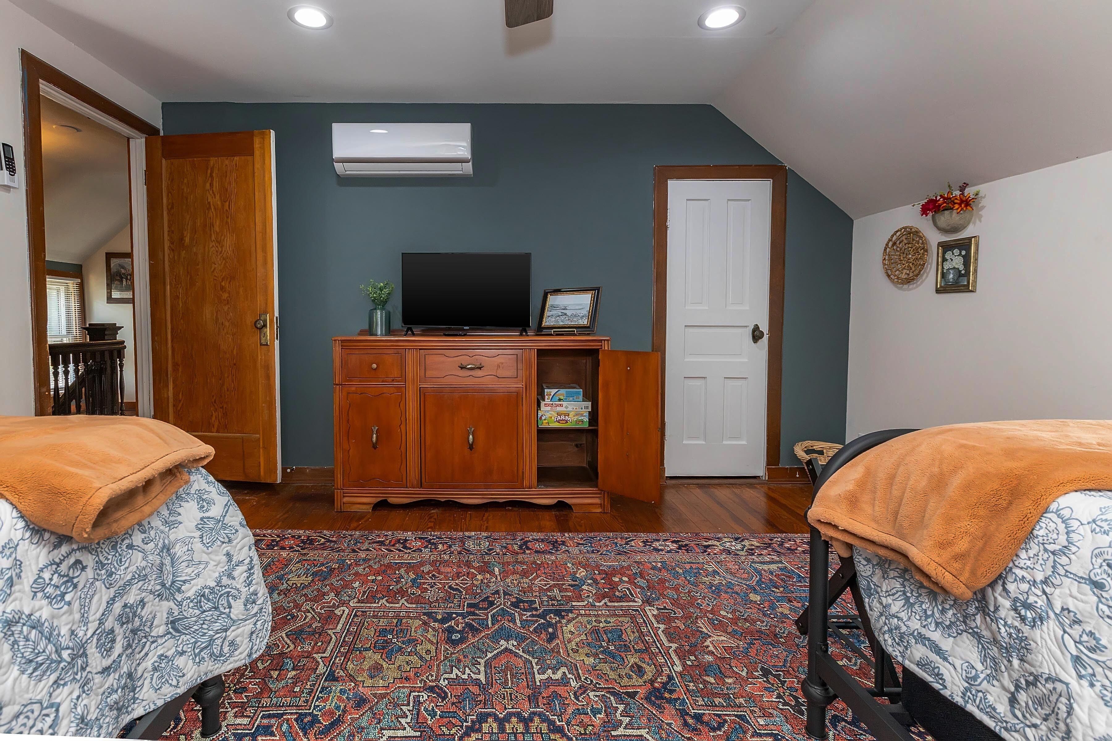A bedroom with two beds, a wooden dresser, a television, and a patterned rug.