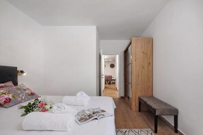 Ein Schlafzimmer mit einem Bett, einer Bank, einem Holzschrank und einem Gang, der zu einem Essbereich führt.