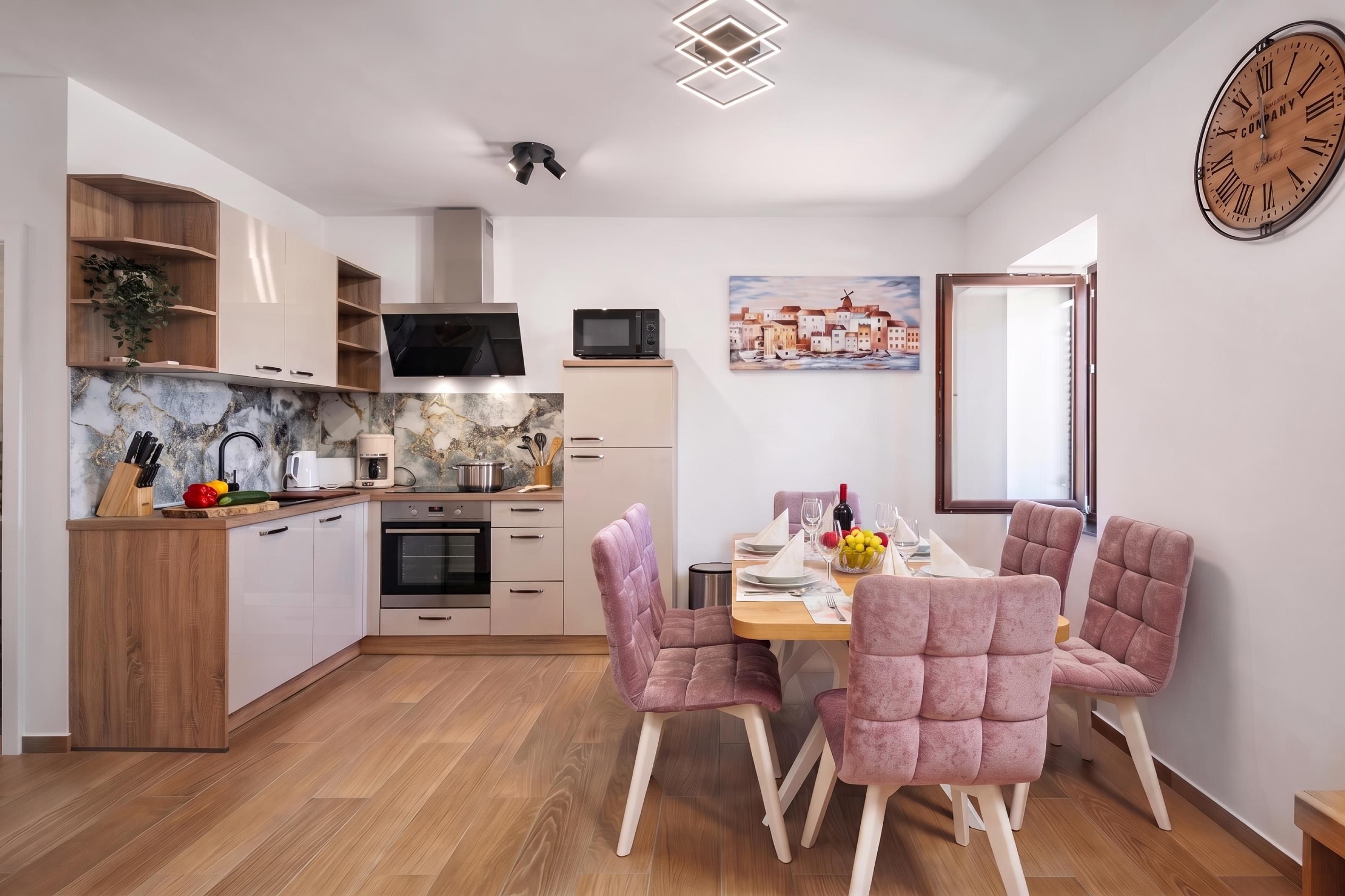 A modern kitchen with wooden cabinets, a microwave, and a dining area with pink upholstered chairs.