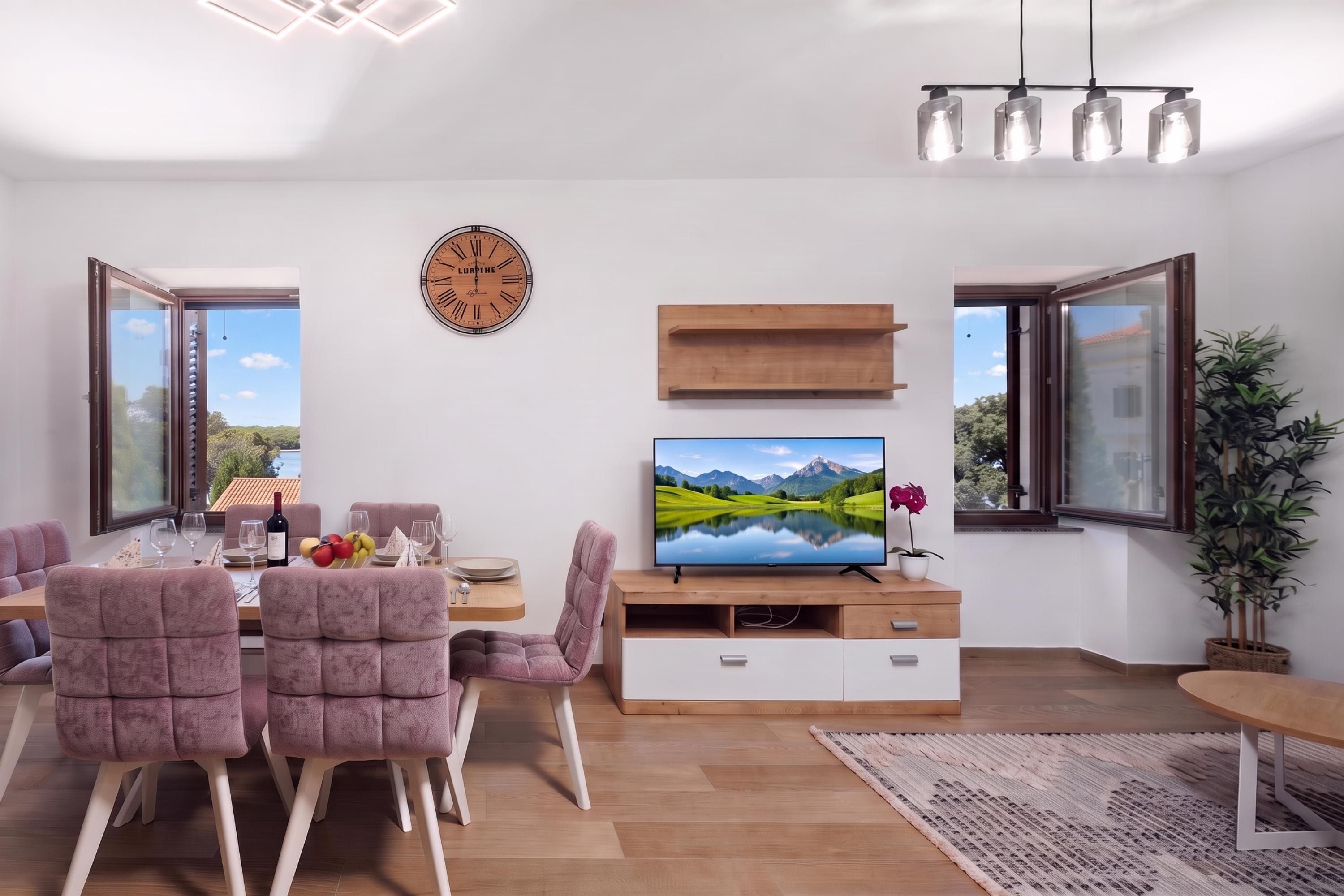 A modern living room with a dining area, a flat-screen TV, a clock, and large windows.