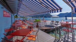 A deck with tables and chairs, overlooking a body of water and mountains. - Pazzallo Panoramica with Balcony and Garage, Lugano, Switzerland (Lugano)