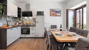 Une cuisine moderne avec des meubles blancs, un pare-feu en marbre et un coin repas comprenant une table en bois et des chaises à revêtement gris.