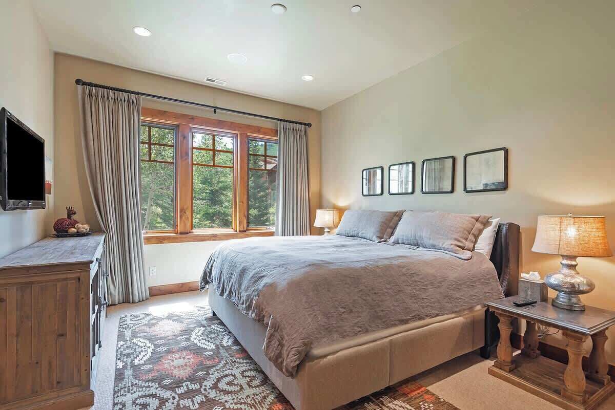 A bedroom with a bed, a TV, a window with curtains, and framed pictures on the wall.