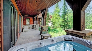 Un jacuzzi con borde de piedra, cubierta de madera y vista a un bosque.