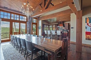 Une salle à manger spacieuse avec une longue table en bois, de nombreuses chaises et un lustre.