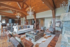 Un vaste espace de vie doté d’un plafond haut, de poutres en bois, d’un lustre, d’une cheminée et d’un mur d’accent en pierre.