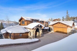 Un chalet enneigé, doté d’une entrée en arc de pierre, d’une façade en bois et d’un garage.