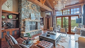 Amplia sala de estar con chimenea de piedra, muebles de cuero y grandes ventanas que ofrecen vistas al exterior.