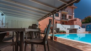 Ein überdachter Außenbereich mit Pool, Holzboden und Gartenmöbeln.