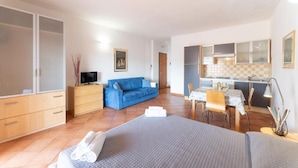 Ein gemütlicher Raum mit Bett, blauem Sofa, kleinem Esstisch, Fernseher und einer Küchenzeile.