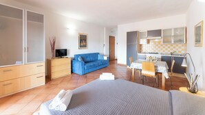 Un dormitorio con cama, un sofá azul, un escritorio con silla y una kitchenette.