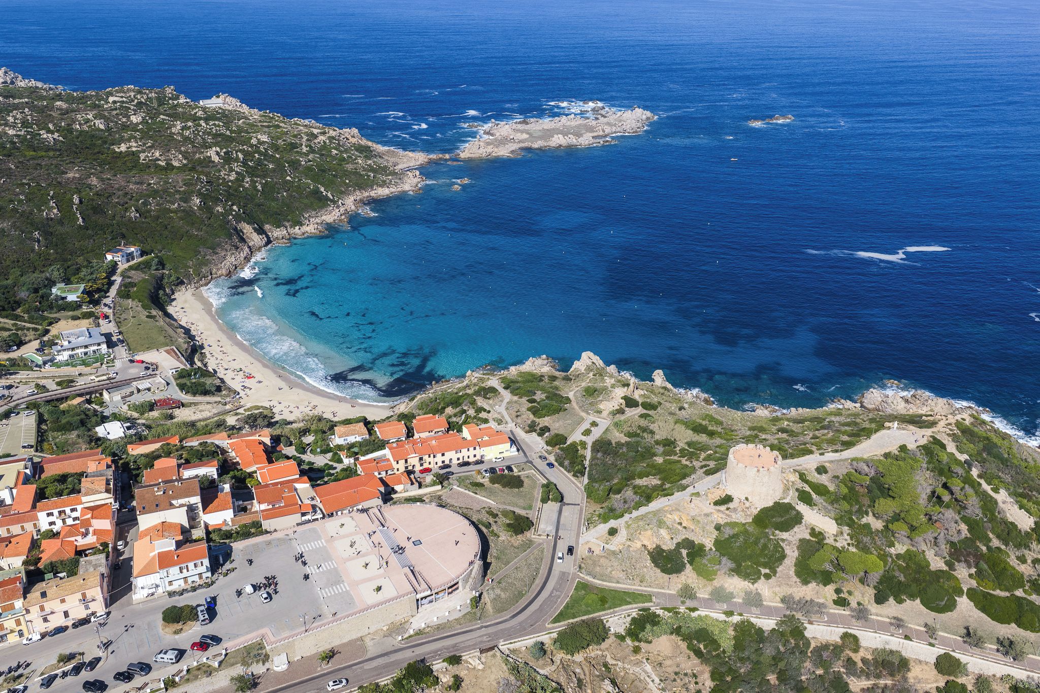 An aerial view of a coastal town with a beach, a fortified structure, and residential buildings.