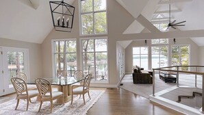 Amplia habitación con una gran mesa de comedor, varias sillas y vistas a un lago a través de ventanas amplias.