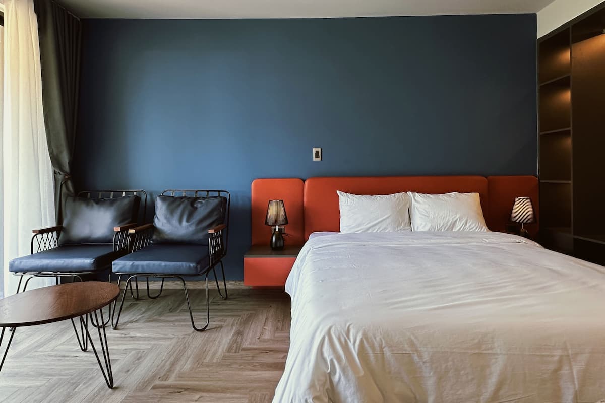Ein Hotelzimmer mit einem großen Bett, zwei Sesseln, einem kleinen Tisch und einem Nachttisch mit Lampen.