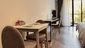 A hotel room with a wooden floor, a dining table with chairs, a bed, an air conditioning unit, and a window with curtains. - TUK TAK SPACES (Da Nang)