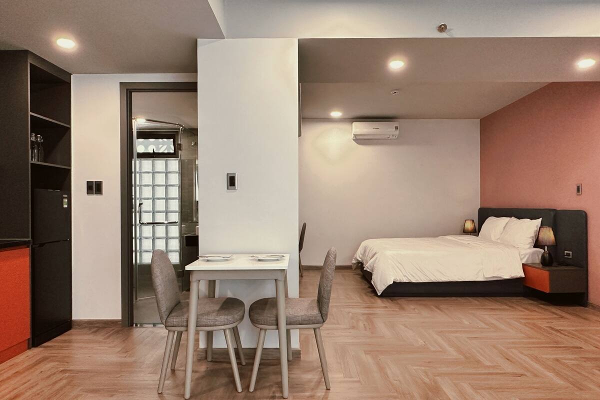 Ein gemütliches Hotelzimmer mit Bett, Nachttisch, Lampe und einer kleinen Sitzecke mit Stühlen.