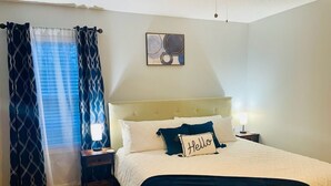 A bedroom with a bed, a nightstand, a bedside lamp, a window with curtains, and a wall art piece. - Family Friendly Home~Pets Welcome-Fenced Yard (Clarksville)