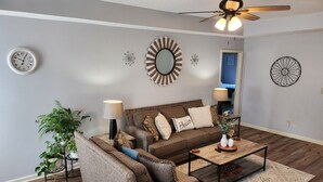 A living room with a brown sofa, two side chairs, a coffee table, a floor lamp, a wall clock, decorative mirrors, and a ceiling fan. - Family Friendly Home~Pets Welcome-Fenced Yard (Clarksville)