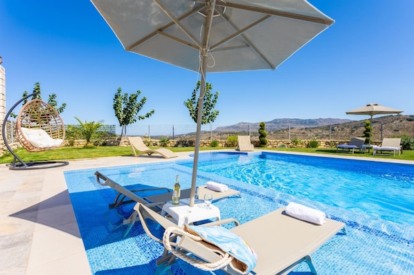 A pool area with lounge chairs, umbrellas, and a view of the mountains.