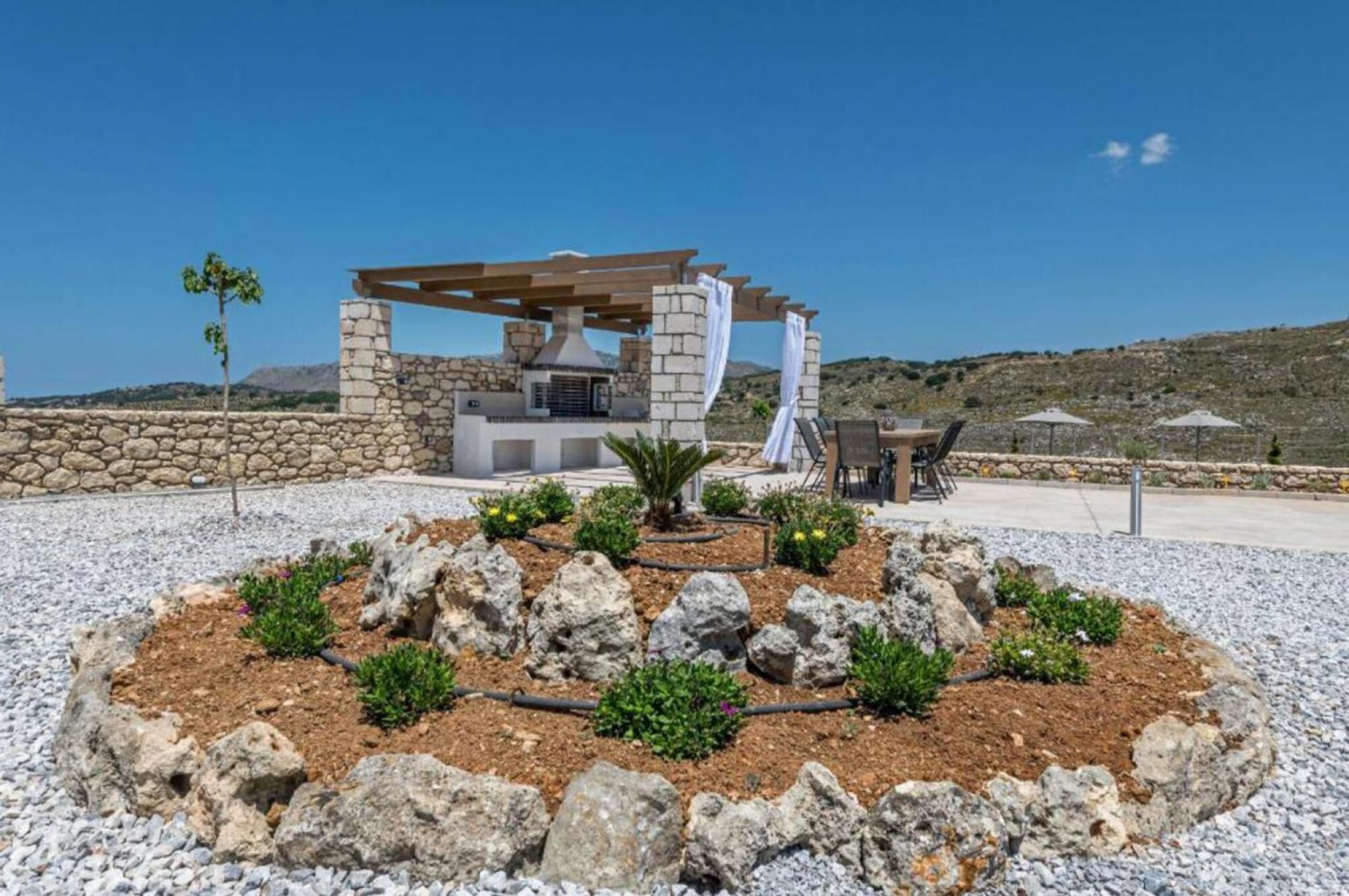 A modern outdoor kitchen with a stone wall and a pergola.