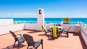 Terraço com mesa e cadeiras, um pilar branco e vista para o mar.