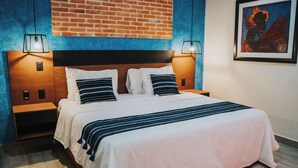 A neatly made bed with a striped blanket, a wooden headboard, and two bedside lamps. - Hotel Casa Puga (Oaxaca)