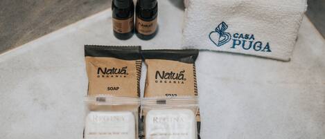 A bathroom setting with a white towel, two bottles of soap, and two soap bars labeled 'Natura Organía'.
