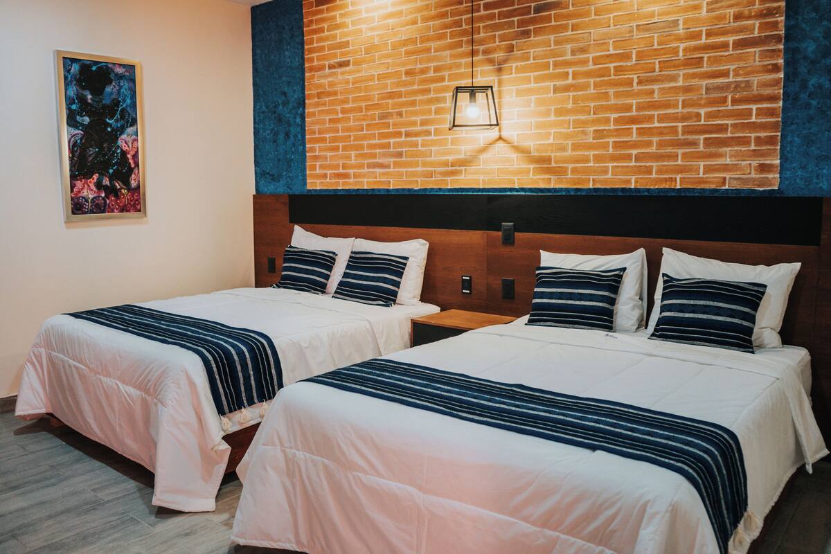 Une chambre d’hôtel avec deux lits, un mur en briques et un tableau.
