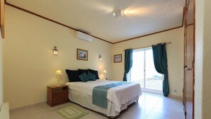 A bedroom with a bed, bedside tables, a window with curtains, and an air conditioning unit. - Villa Brejos in Albufeira (Albufeira)