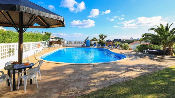 A swimming pool with lounge chairs and a table, surrounded by a brick patio and greenery. - Villa Brejos in Albufeira (Albufeira)
