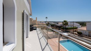 A balcony with a pool, clear skies, and a view of a residential area. - Villa Quinta do Jolu (Albufeira)