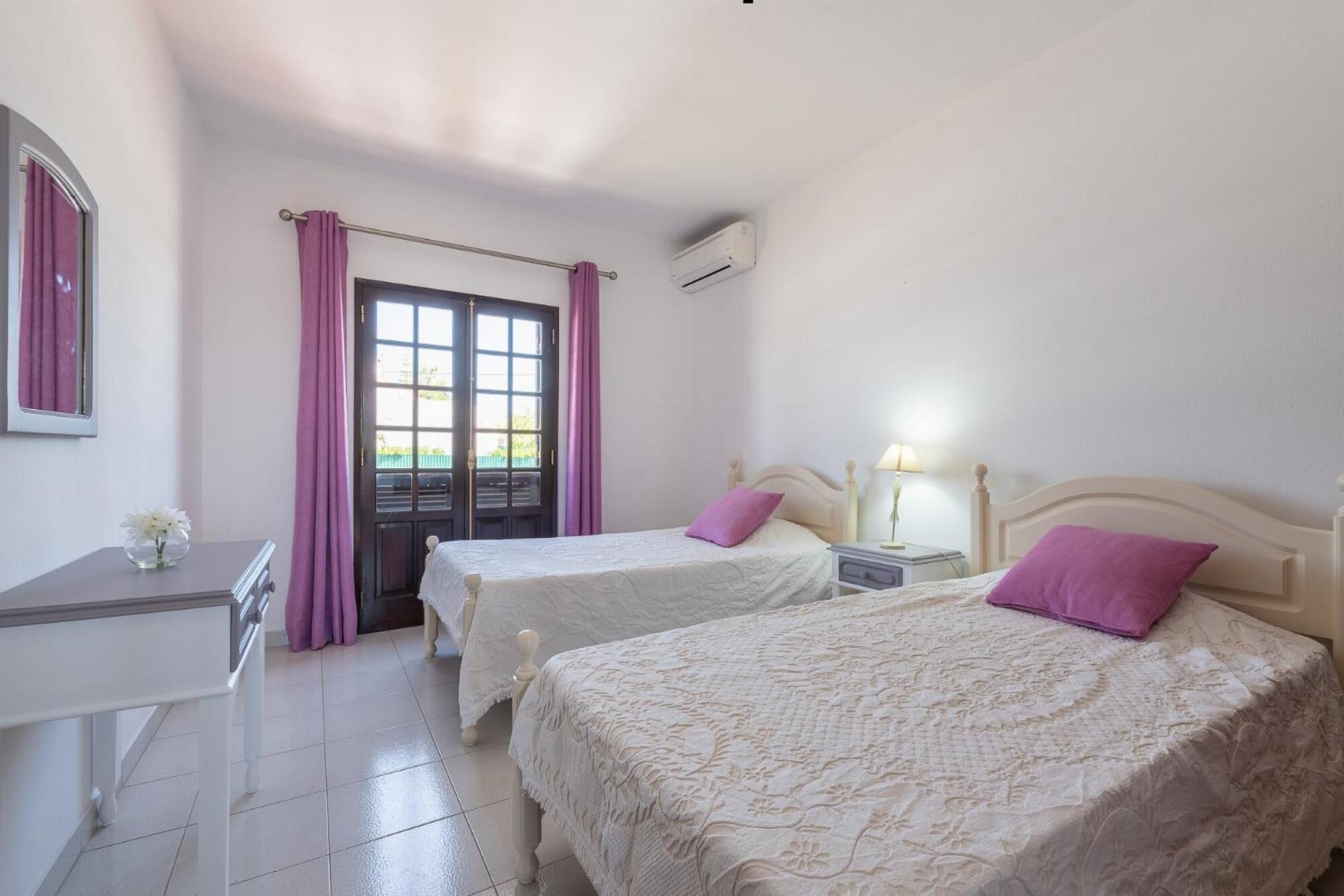 A bedroom with two beds, a desk, and a window with curtains.