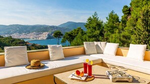 Une terrasse avec un canapé et une table, offrant une vue sur une ville côtière et la mer.