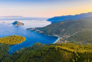 An aerial view of a coastal area with a small town nestled among hills and a large bay with boats.