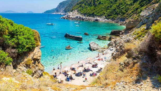 Une plage côtière bordée d’une eau turquoise et limpide, avec un terrain rocheux et une végétation luxuriante.