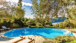 Une piscine entourée d’escaliers en pierre et de chaises longues, avec des arbres et une vue sur un lac.
