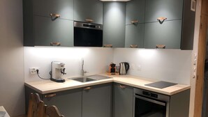 A compact kitchen with dark cabinets, a built-in oven, a coffee maker, and a kettle. - Lauzière Dessus 22 - Crève Coeur (LES AVANCHERS VALMOREL)