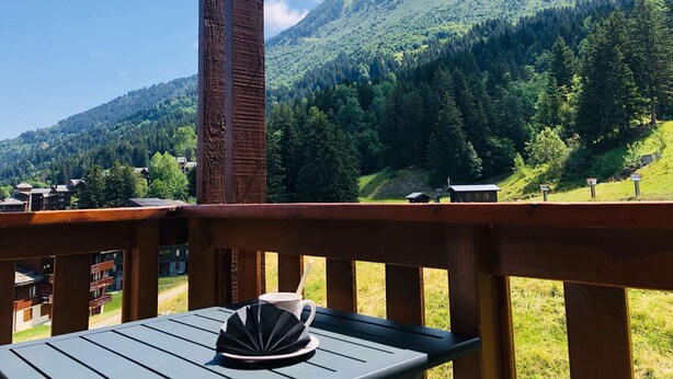 A wooden deck with a table and a cup, overlooking a mountainous landscape with a clear sky. - Lauzière Dessus 22 - Crève Coeur (LES AVANCHERS VALMOREL)