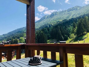 A wooden deck with a table and a cup, overlooking a mountainous landscape with a clear sky. - Lauzière Dessus 22 - Crève Coeur (LES AVANCHERS VALMOREL)