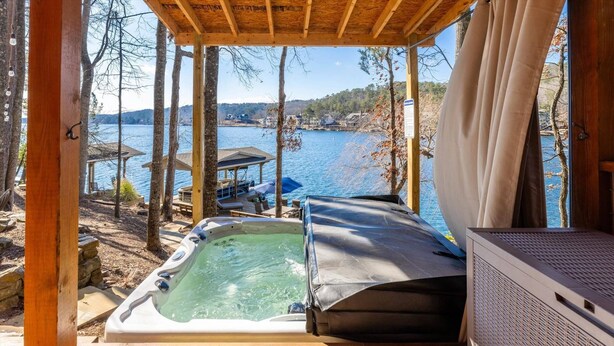 A wooden deck with a hot tub, a covered seating area, and a view of a lake and hills. - Lake Front Home w/Private Dock, Kayaks, Fire Pit & Hot Tub | Community Pool & Tennis (Waleska)
