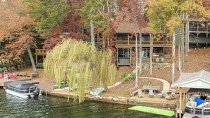 A lakeside cabin with a dock, outdoor seating, and a weeping willow tree. - Lake Front Home w/Private Dock, Kayaks, Fire Pit & Hot Tub | Community Pool & Tennis (Waleska)
